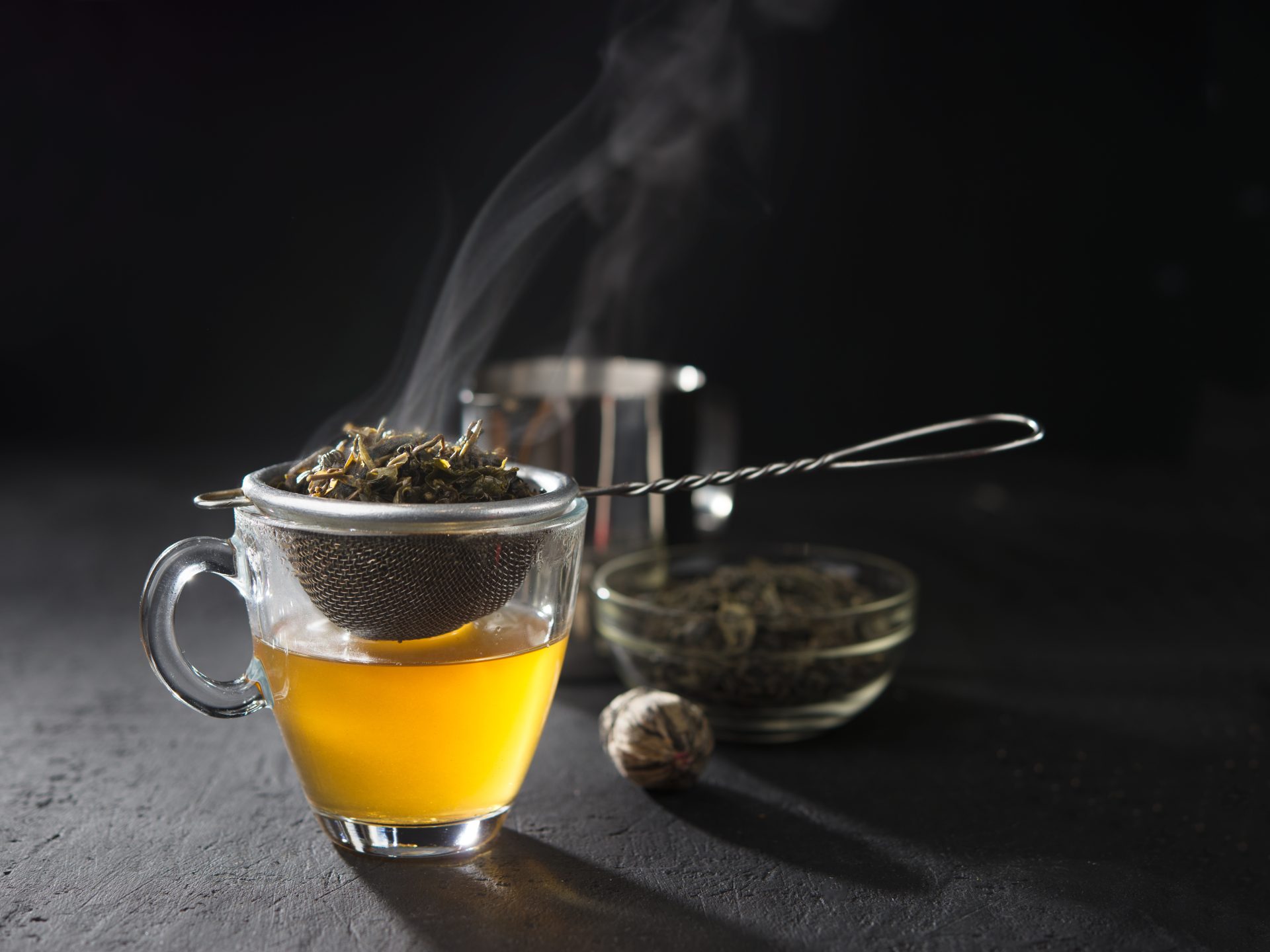Strainer over cup with steaming yellow tea.